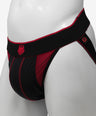 A black and red jockstrap with a prominent red stripe and a small emblem on the front, displayed on a mannequin.